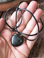 Heart obsidian pendant on black cord in hand showing size and texture