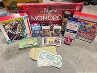 Group shot showing entire lot including Monopoly box, two puzzle boxes, pick-up sticks tube, playing cards, yo-yo, keychain, toy money