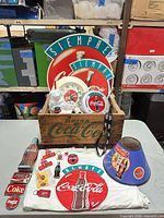 Full lot view showing crate, clocks, signage, lamp shade, T-shirt, pins and other items