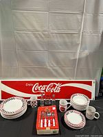 Overview of dinnerware, mugs, shakers, boxed flatware and metal sign