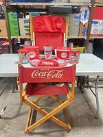 Group shot of director chair with Coca-Cola tins, hat, cup and cooler bag displayed