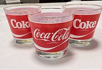 Three clear glass tumblers with red Coca-Cola logo