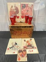 Full lot: crate, two clear glasses, four red tumblers, four advertisement prints