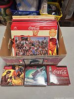 Box of assorted Coca-Cola wall calendars and three boxed daily calendars visible