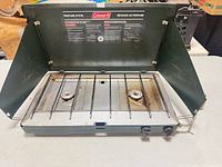 Stove open showing two burners, grate, lid/windshields