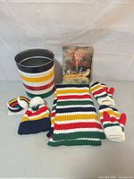 Full lot showing striped tin, book, scarf, hat, mittens, earmuffs