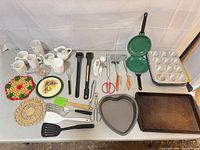 Entire lot laid out showing cookware, bakeware, utensils, mugs, trivets