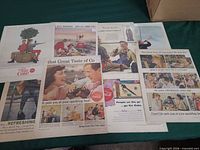 Group of nine assorted 1950s Coca-Cola magazine ad pages laid out on table
