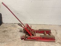 side view of red motorcycle lift jack showing frame, casters and handle