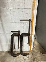 Both C-clamps leaning against wall beside yardstick for scale