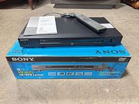 Player resting on original box with manual, remote, power cord visible