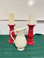 Pitcher centered between two red candlesticks with candles on green cloth