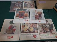 All seven Coca-Cola ads laid out on table