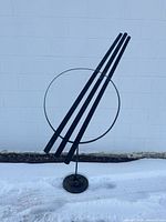 Full view of sculpture front angle showing circular ring and three rods on base