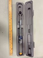 Torque wrench inside open grey storage case next to ruler