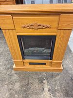 Front view of light oak electric fireplace mantel showing decorative applique and firebox