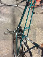 Left side view showing teal frame, crankset, toe-clip pedal and rear rack