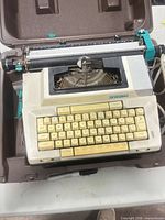 Overall view of the Smith-Corona Coronamatic 2200 typewriter inside its brown carrying case showing keyboard, carriage and power cord
