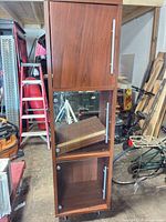 Full front view of tall cherry veneer display cabinet showing wood upper door, two glass doors, metal handles, casters
