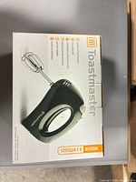 Front of retail box showing image of black Toastmaster hand mixer model TM-300HMCN