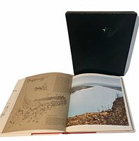 Book open displaying illustrated and photo pages beside black slipcase