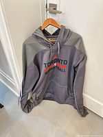 Front view of gray Adidas Toronto Raptors pullover hoodie on hanger