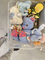 Bin with multiple plush animals including blue patchwork bear, white bear, green frog, blue bunny