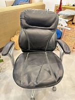 Front view of black faux leather executive office chair showing seat, backrest and armrests with wear