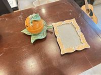 Both items on table: orange covered dish on leaf saucer and peach ceramic picture frame