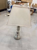 Full view of table lamp showing mirrored base, white square shade, power cord
