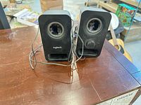 Front view of both Logitech speakers showing drivers, slots, volume knob