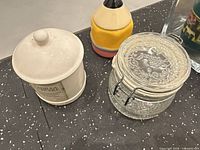 Group view showing ceramic Vanilla Cupcake jar, clear glass embossed canister, and conical ceramic container