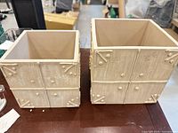 Both square distressed beige resin planters side by side showing size difference and panel design
