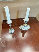 Pair of mixed metal candlestick holders with candles showing size difference and condition