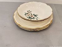 Stack of five floral porcelain pieces showing scalloped gold rims