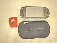 Front view of Sony PSP console beside red PlayStation memory card and black PSP soft case
