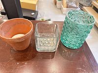 front view of three vessels (terracotta pot, clear glass vase, green glass vase)
