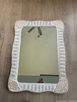 Full view of rectangular white wicker wall mirror on wooden floor