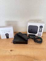 Apple TV 4K box, Roku XD player with remote and power adapter, Chromecast box, cables on tabletop