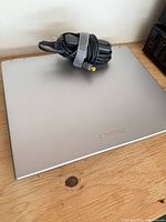 Closed Lenovo laptop showing silver lid and Lenovo logo with AC power adapter placed on top