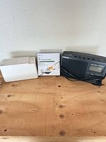 All three items on tabletop: APC UPS, boxed cord cover, Sangean radio