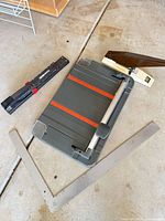 All four items displayed on floor: trimmer, long-reach stapler, lever stapler, framing square