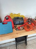 Overall lot on bench showing cords, charger, pipe wrench, rope, fuel can, bit case