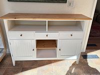 Front view of white sideboard showing natural wood top, open cubbies, three drawers, open shelf, two doors