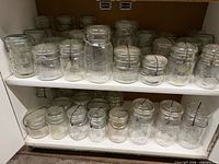Two shelves filled with clear glass canning jars, all with wire bales and glass lids