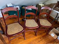 Three wooden chairs with cane seats on hardwood floor