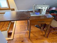 Singer sewing machine installed in wood cabinet with drop leaf
