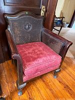 Front view of dark wood armchair with cane back, red cushion, castered legs