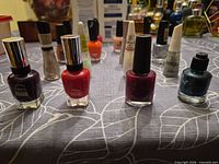 Front row: Sally Hansen deep purple, Sally Hansen red, CND burgundy, teal glitter; background additional bottles