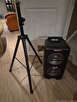 Full view of speaker on floor beside folded tripod stand